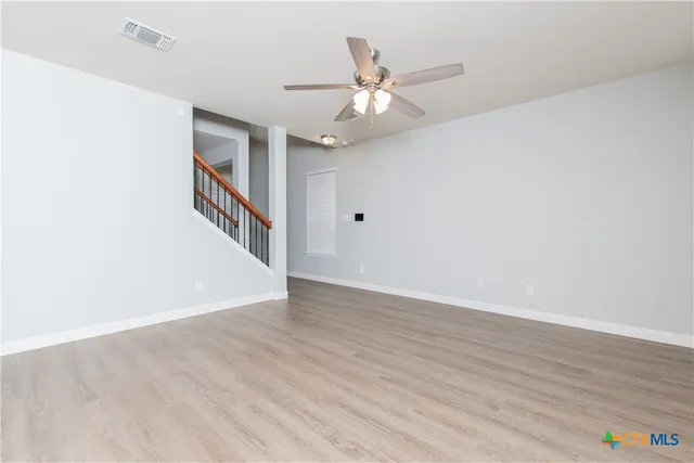 a view of an empty room with wooden floor and a ceiling fan