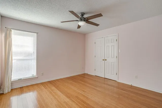 an empty room with wooden floor fan and windows