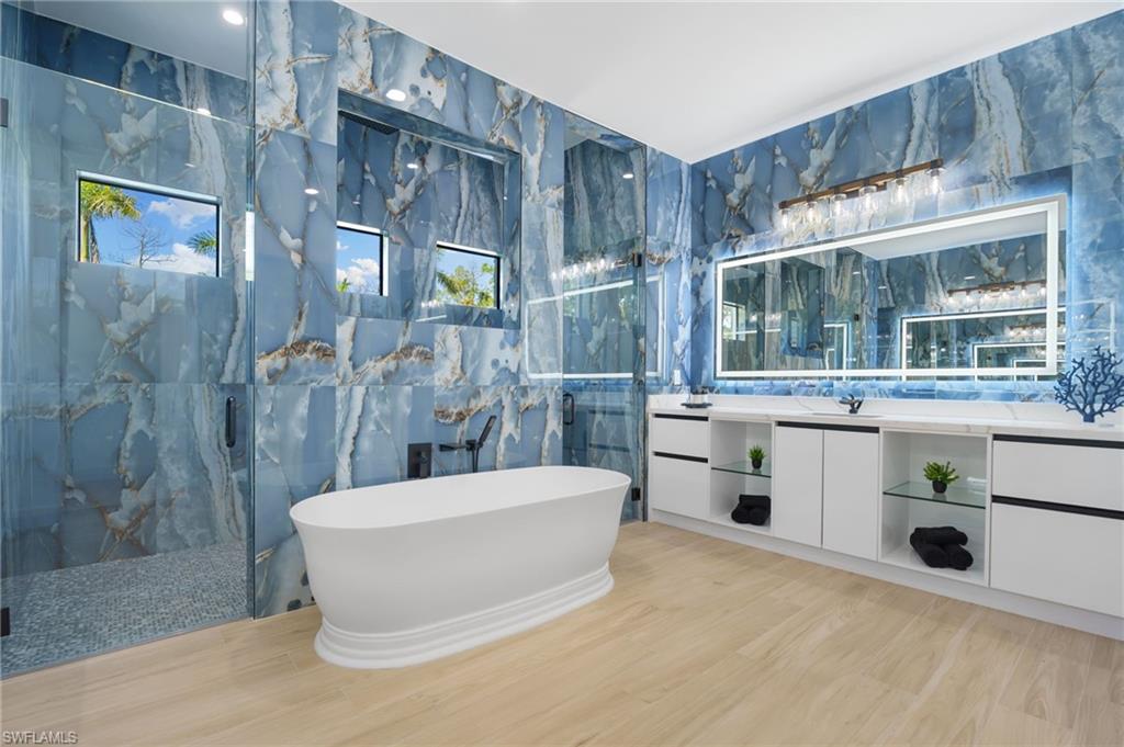 7040 Sable Ridge Lane Naples, FL 34109 - Photo 27 of 50 spa-like bathroom adorned in marbled tile, complete with dual vanities, an oversized shower, and a freestanding soaking tub.