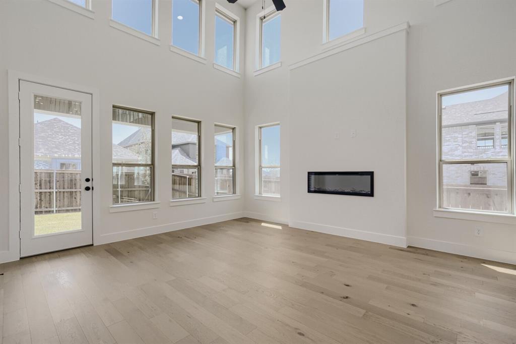 824 Stone Grv Road Lavon, TX 75166 - Photo 3 of 26 Living area featuring light wood-finish flooring, high ceilings, a wall-mounted linear fireplace, and abundant natural light from multiple windows and a glass-paneled door