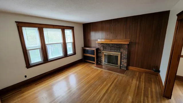 an empty room with wooden floor fireplace and windows