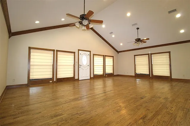 an empty room with wooden floor fan and windows