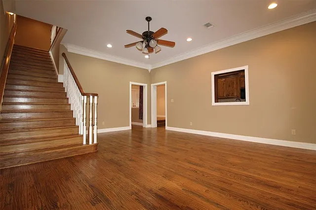 a view of an empty room with wooden floor and a ceiling fan