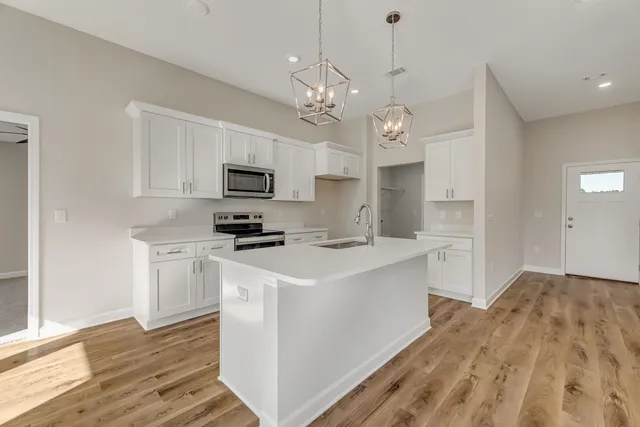 a kitchen with a sink a microwave oven a stove and white cabinets with wooden floor