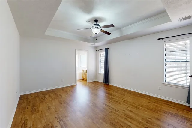 an empty room with wooden floor ceiling fan and windows