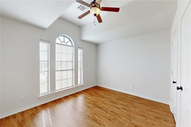 an empty room with wooden floor fan and windows