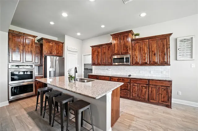 a kitchen with granite countertop lots of wooden cabinets a sink dishwasher a dining table and chairs