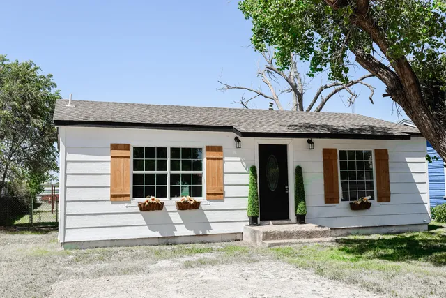 a front view of a house with a large tree and table and chairs in patio