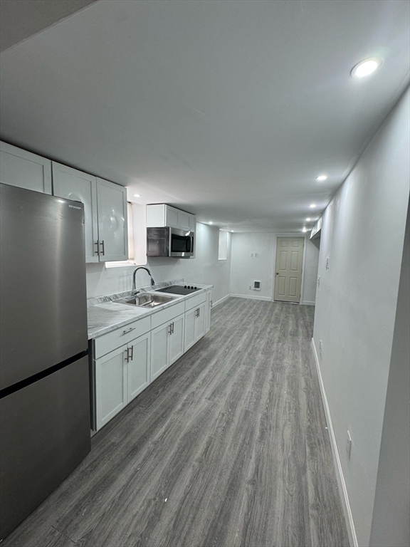 a large kitchen with a refrigerator a sink dishwasher a stove and white cabinets with wooden floor