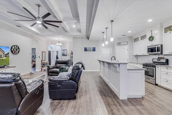 a large white kitchen with stainless steel appliances kitchen island granite countertop a stove a refrigerator a oven with white cabinets and wooden floor