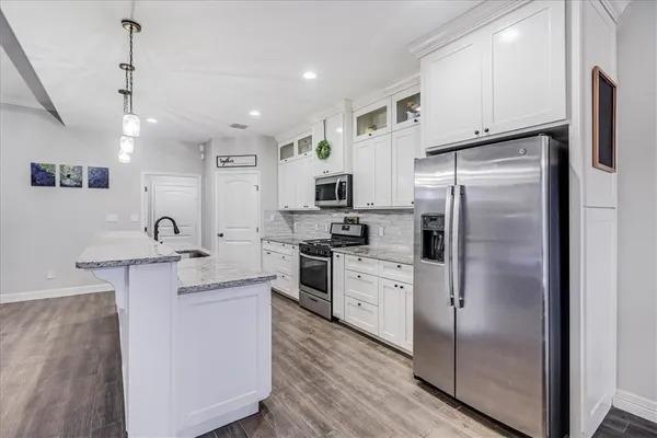 a kitchen with stainless steel appliances granite countertop a stove top oven a sink dishwasher a dining table and chairs with wooden floor