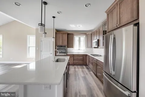 a large kitchen with a refrigerator a sink dishwasher a stove and white cabinets with wooden floor