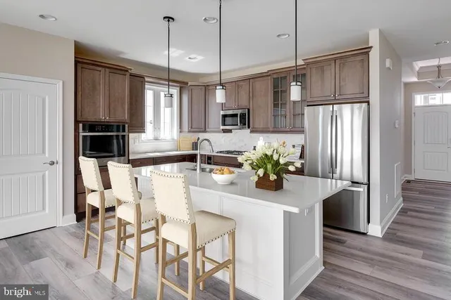 a kitchen with stainless steel appliances granite countertop a refrigerator a oven a sink a dining table and chairs with wooden floor