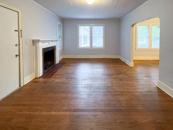 an empty room with wooden floor fireplace and windows