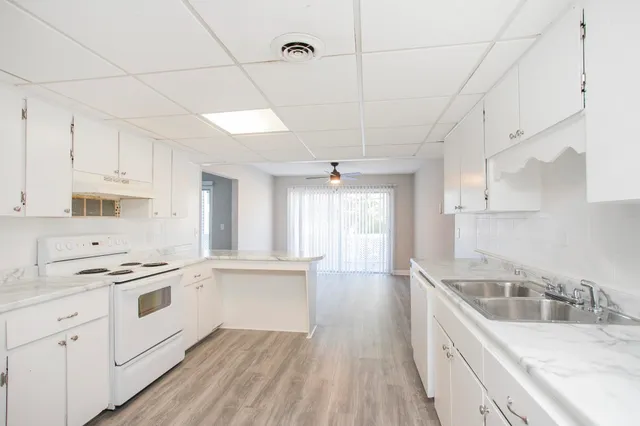 a kitchen with stainless steel appliances granite countertop a sink stove and white cabinets with wooden floor