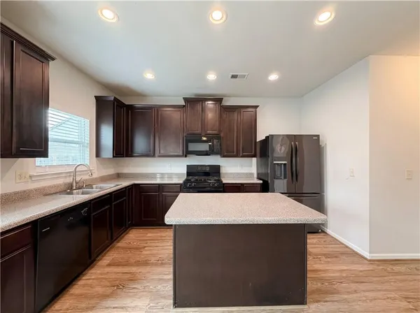 a large kitchen with stainless steel appliances kitchen island a sink dishwasher a stove a refrigerator and a oven with wooden floor