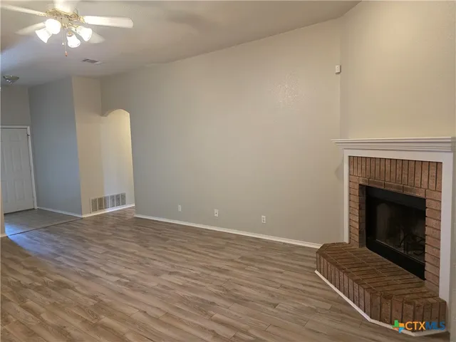 a view of an empty room with wooden floor and a fireplace