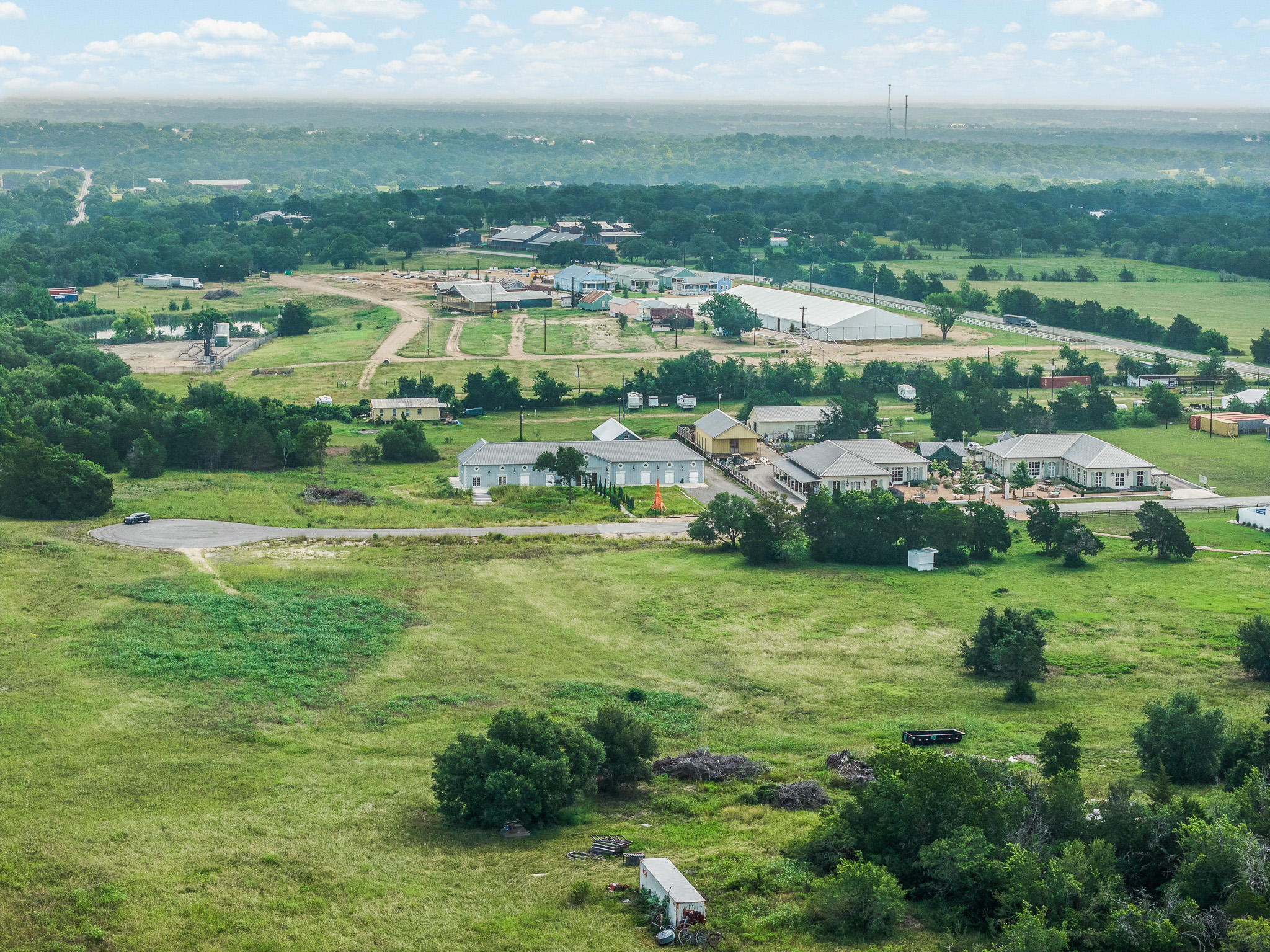109 Compound Lane Round Top, TX 78954 - Photo 6 of 23 An aerial panorama reveals a vast, green landscape dotted with residential structures and commercial facilities, offering diverse development opportunities.