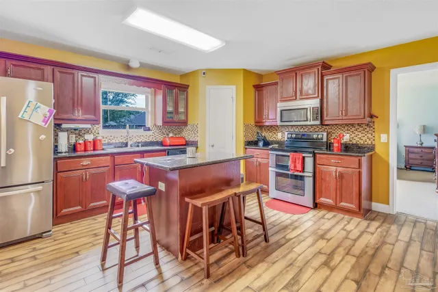 a kitchen with stainless steel appliances granite countertop a stove top oven a sink dishwasher a dining table and chairs with wooden floor