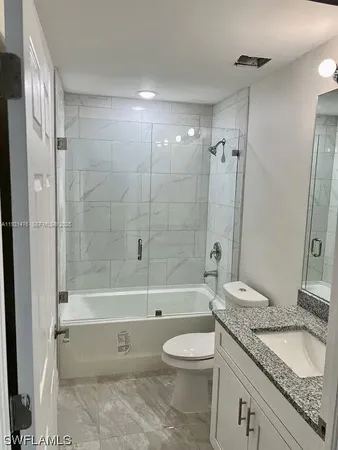 a bathroom with a granite countertop toilet a sink a shower and a mirror