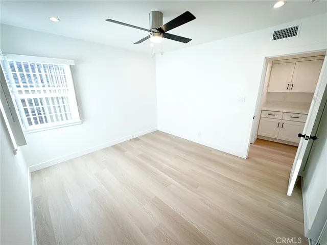 an empty room with wooden floor a ceiling fan and windows