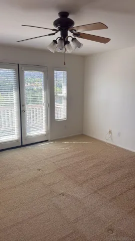 an empty room with chandelier fan and windows