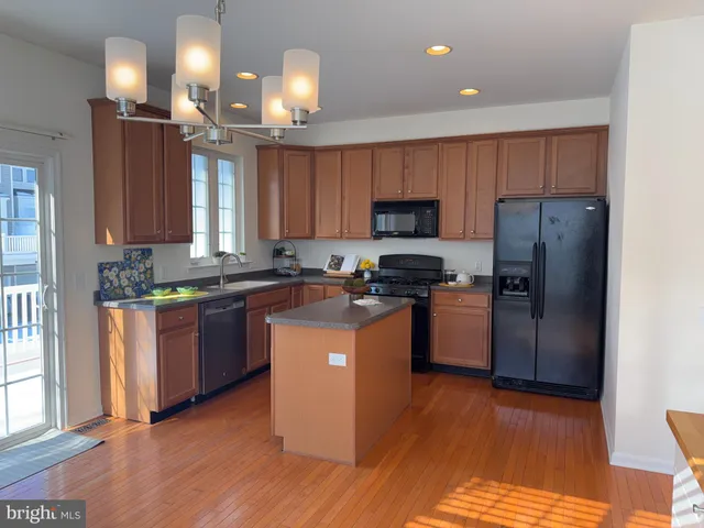 a kitchen with stainless steel appliances granite countertop a refrigerator a sink dishwasher a stove a microwave oven and a dining table with wooden floor
