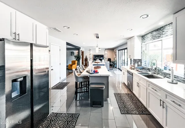a kitchen with stainless steel appliances kitchen island granite countertop a refrigerator a sink dishwasher and white cabinets with wooden floor
