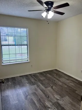 an empty room with wooden floor fan and windows