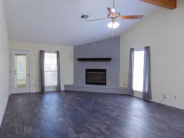 an empty room with wooden floor a ceiling fan a fireplace and windows