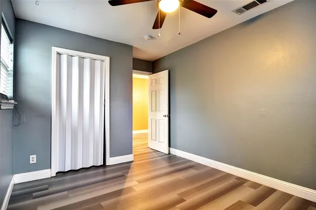 an empty room with wooden floor chandelier fan and windows