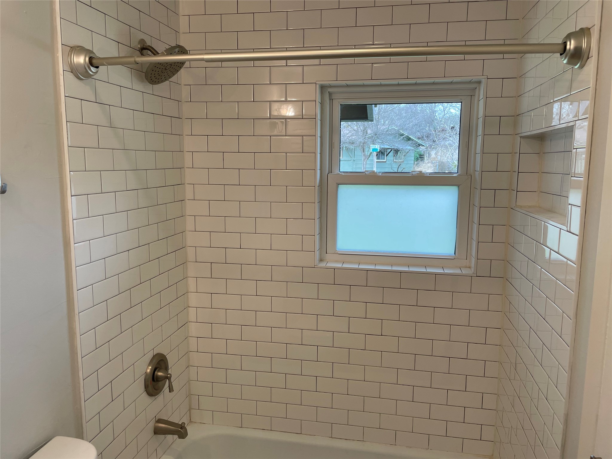 4619 Jinx Avenue, Unit A Austin, TX 78745 - Photo 12 of 21 Bathtub with white subway tile surround, built-in recessed niche, brushed nickel fixtures, and a window with frosted lower pane