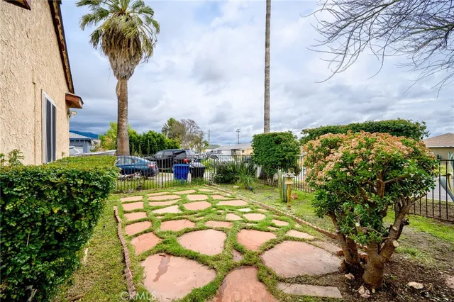 a view of a white house with a small yard plants and large trees