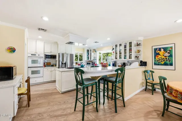 a dining area with stainless steel appliances kitchen island granite countertop a dining table chairs and a refrigerator