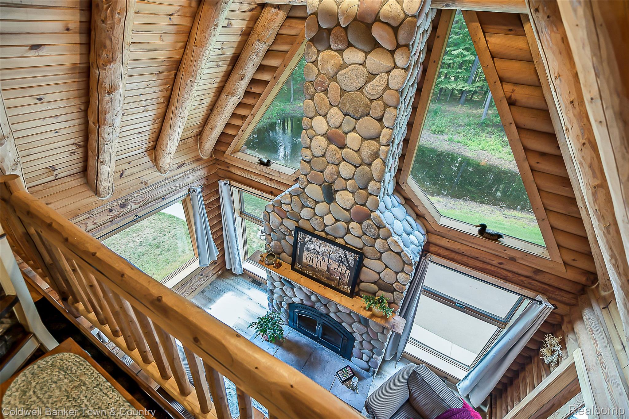 7023 Munsell Road Howell, MI 48843 - Photo 41 of 55 Vaulted wood-paneled ceiling with exposed log beams, stone-clad fireplace with wood mantle, wood-finish flooring, and expansive windows