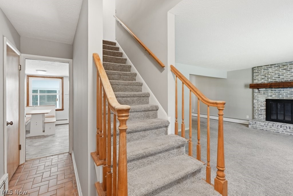 136 Pinehurst Road Munroe Falls, OH 44262 - Photo 22 of 48 Carpeted staircase with wooden banister, brick fireplace with wood mantel, light gray walls, and terracotta-style flooring