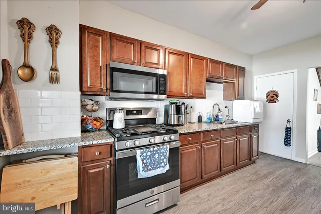 a kitchen with stainless steel appliances granite countertop a stove top oven a sink dishwasher and a microwave oven with wooden cabinets