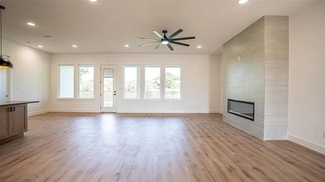 an empty room with wooden floor a ceiling fan a fireplace and windows