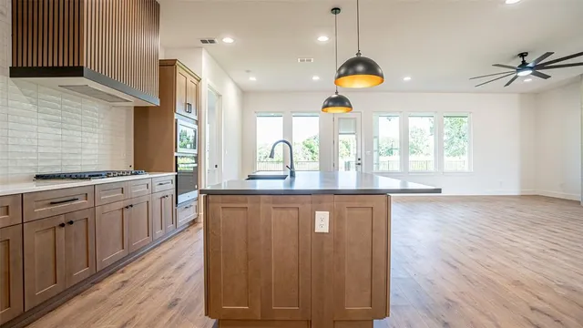 a kitchen with kitchen island granite countertop a stove a sink and white cabinets with wooden floor