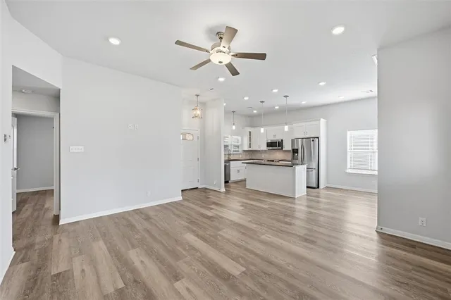 a view of an empty room with kitchen view and wooden floor