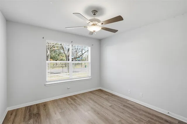 an empty room with wooden floor fan and windows