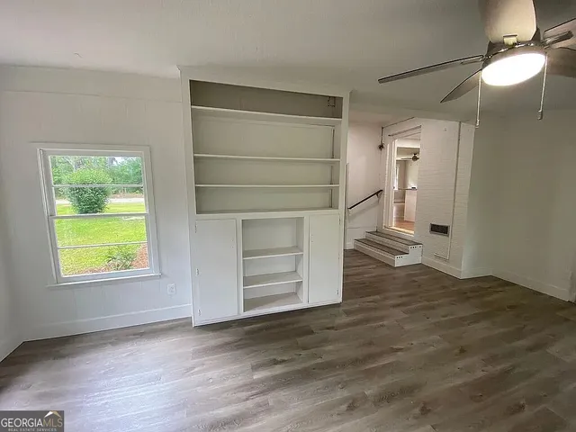 an empty room with wooden floor cabinet and windows