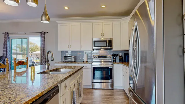 a kitchen with stainless steel appliances granite countertop a refrigerator a stove and a sink with wooden floor