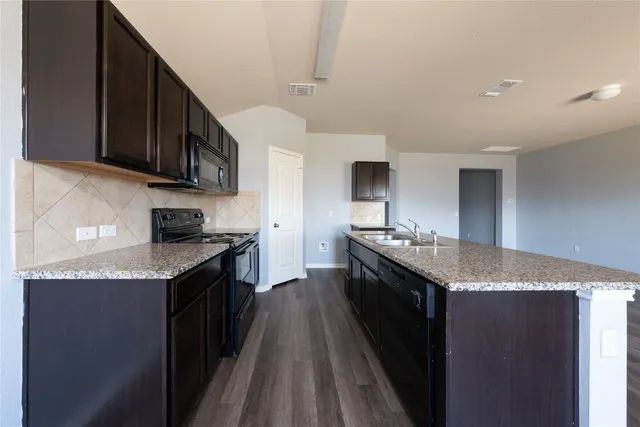 a kitchen with granite countertop stainless steel appliances a sink a stove top oven a counter space and cabinets