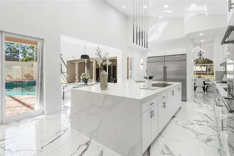 a large white kitchen with kitchen island a large counter top space a sink stainless steel appliances and cabinets