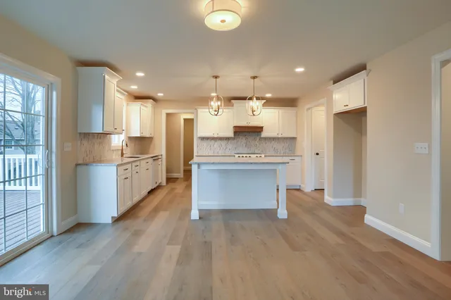 a large kitchen with stainless steel appliances kitchen island granite countertop a stove a sink a refrigerator and white cabinets with wooden floor