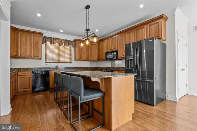 a kitchen with stainless steel appliances granite countertop a refrigerator a stove a sink dishwasher a dining table and chairs with wooden floor