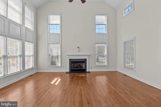 a view of an empty room with wooden floor fireplace and a window