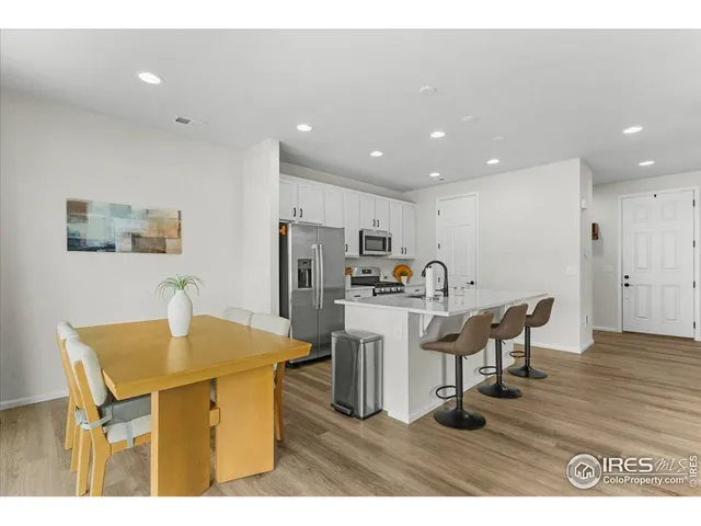 a kitchen with stainless steel appliances kitchen island granite countertop a refrigerator a sink a stove and white cabinets with wooden floor