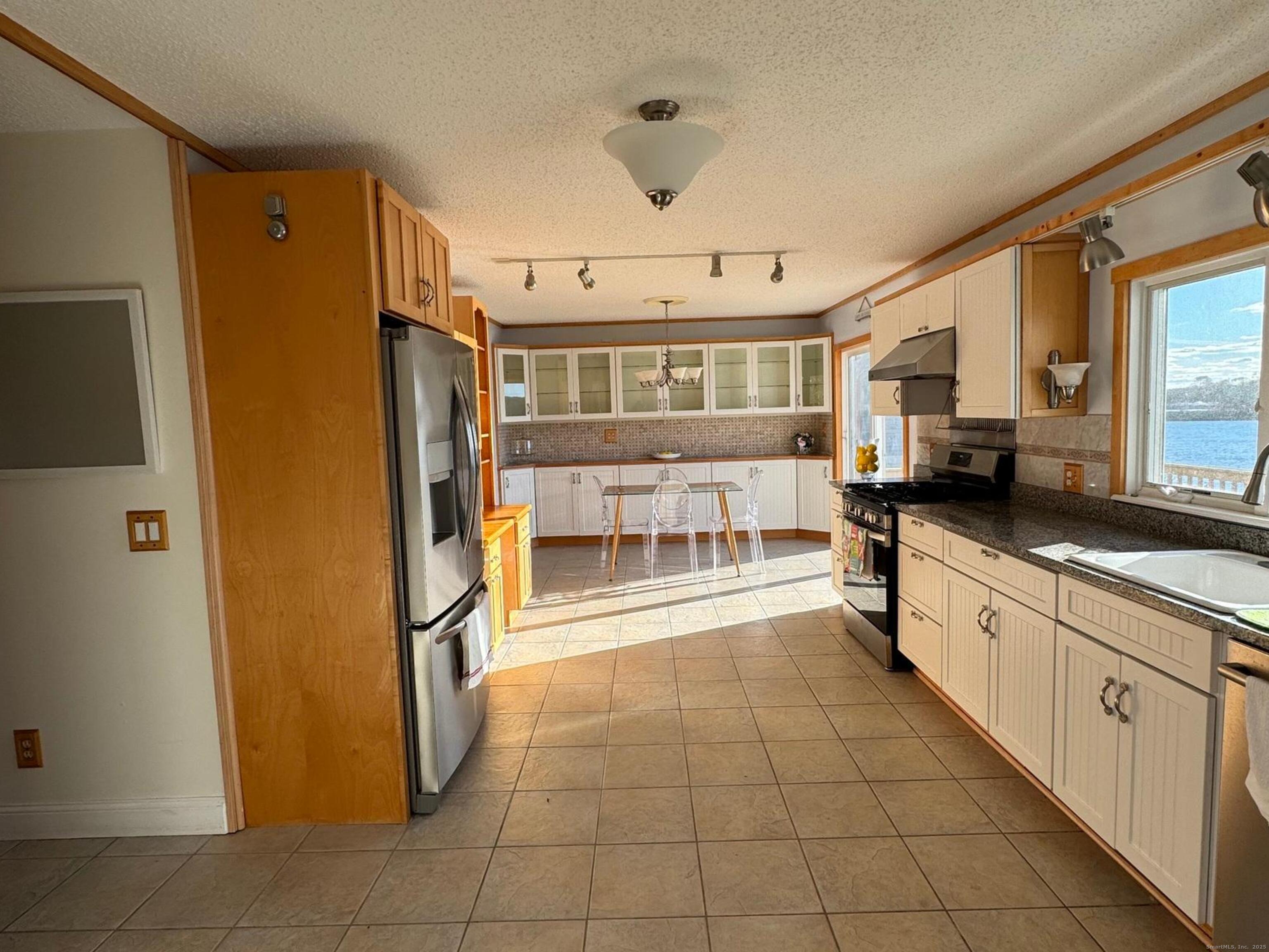 123 Seneca Drive Groton, CT 06340 - Photo 8 of 25 a large white kitchen with granite countertop a refrigerator a sink a stove and white cabinets